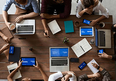 a group of people sitting around a table with laptops