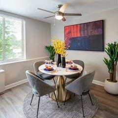 A dining room with a round table set for two and a painting on the wall.