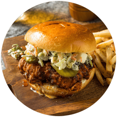 A chicken sandwich with coleslaw and pickles on a wooden board.