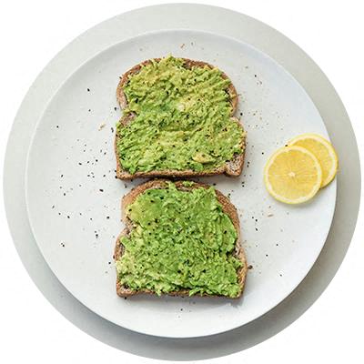 Two slices of toast topped with green avocado spread and served with lemon slices on a white plate.