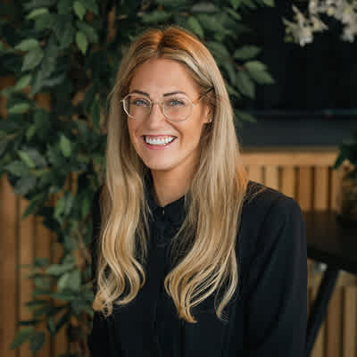 A woman with long blonde hair and glasses is smiling.