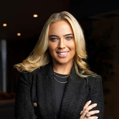 A woman with blonde hair wearing a black blazer and a gold necklace.