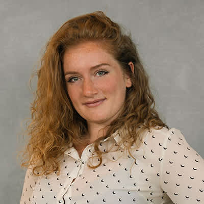 A woman with curly hair wearing a white blouse with black dots.
