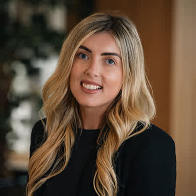 A woman with long blonde hair and a black top is smiling.