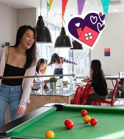 A woman is playing pool in a room with hanging decorations.