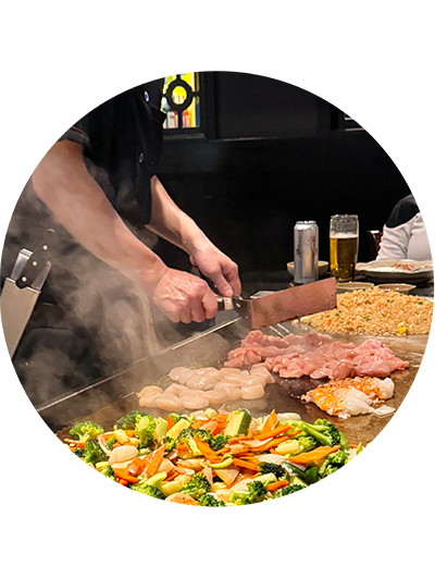 A person is cooking meat and vegetables on a grill.