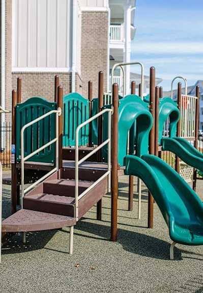 A playground with a green slide and a brown staircase.