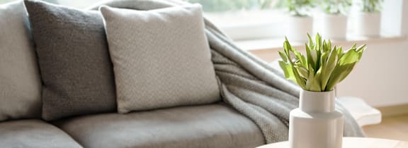 A grey couch with a white vase on a wooden table.