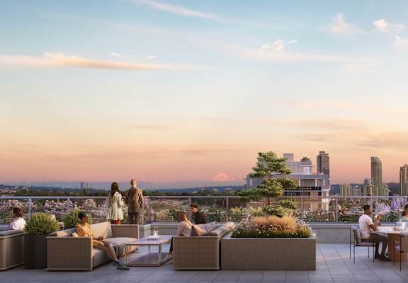 A group of people are sitting and standing on a rooftop terrace with a city skyline in the background.
