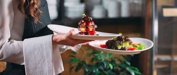 A person holding two plates with food on them.