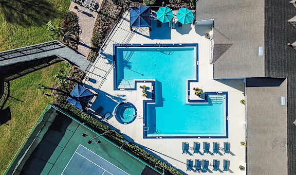 An aerial view of a swimming pool surrounded by lounge chairs and a tennis court.