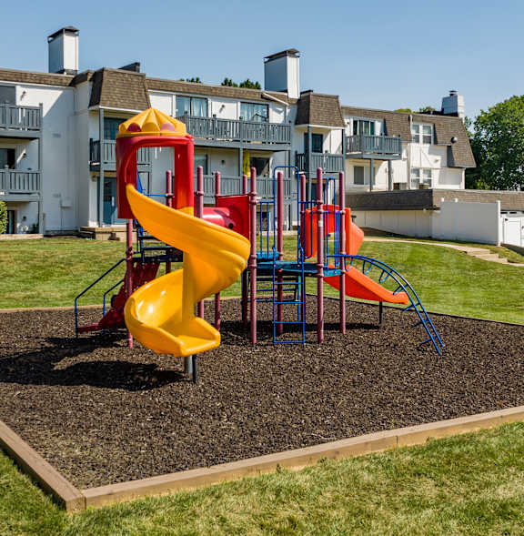 A playground with a yellow slide and a red slide.