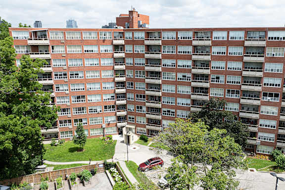 A red car is parked in the driveway of a large apartment building.