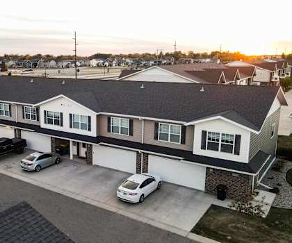 A sunset view of a residential building with cars parked in front.