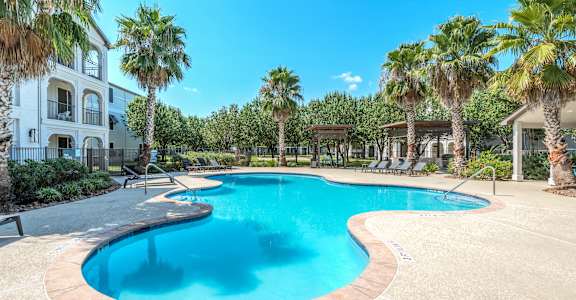 A large swimming pool surrounded by palm trees and a white building.