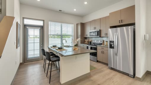a kitchen with stainless steel appliances and a large island with chairs at Slate at Fishers District, Fishers, 46037