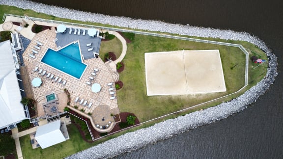 A house with a pool and a sandy area is surrounded by a water body.