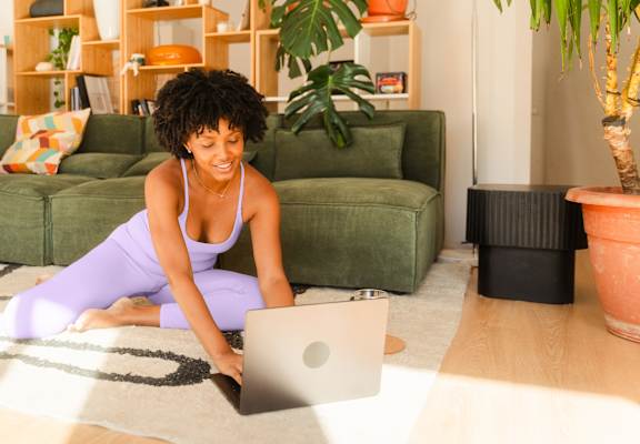 A woman in a purple dress is sitting on the floor using a laptop.