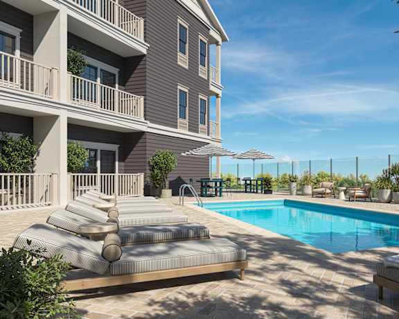 A large swimming pool is surrounded by a sun lounger and a building.