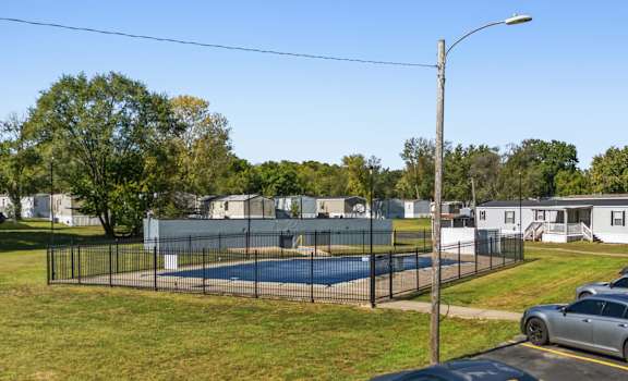 A pool surrounded by a fence with a car parked in front.