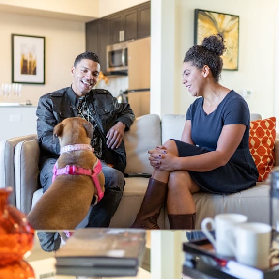 A man and woman sitting on a couch with their dog at Yorkshire Apartments.