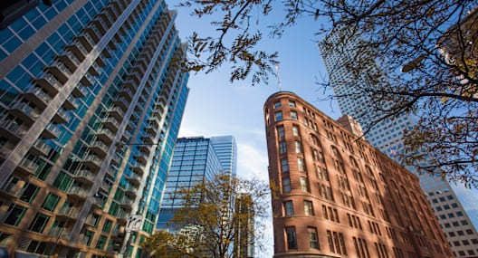 A tall brown building stands between a blue glass building and a shorter brown building.