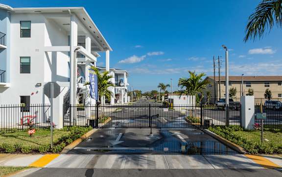 A street view of a residential area with white buildings and a black gate.