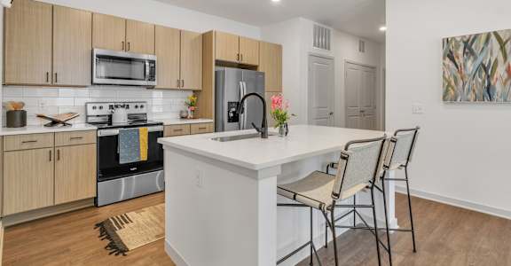 a kitchen with a large island with a white counter top and three chairs