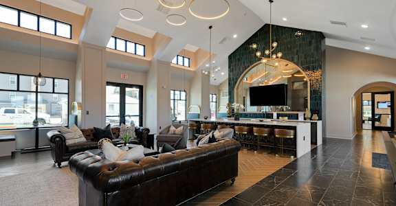 A large, modern living room with a black leather couch and a bar area.