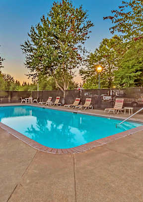 A pool surrounded by trees and chairs.