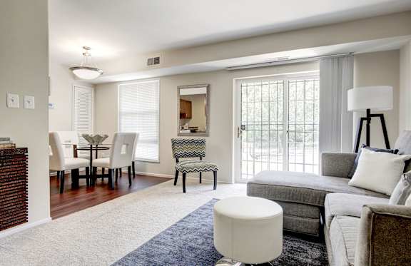 A well-lit living room with a grey couch and a white ottoman.