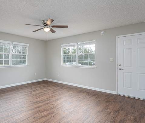 an empty living room with wood floors and a ceiling fan