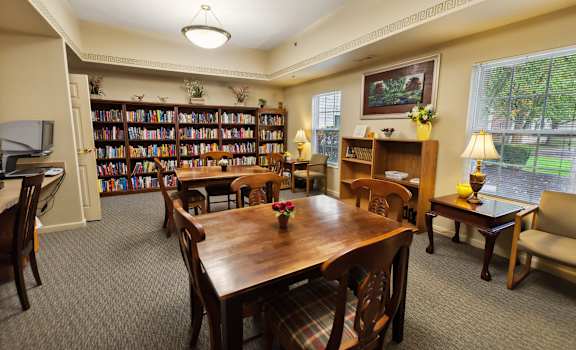 A room with a long table surrounded by chairs and a bookshelf filled with books.