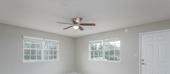 an empty bedroom with a ceiling fan and three windows