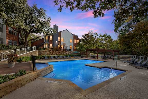 A swimming pool surrounded by a stone wall with a building in the background.
