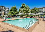 Thumbnail 1 of 20 - A large swimming pool surrounded by trees and apartment buildings.
