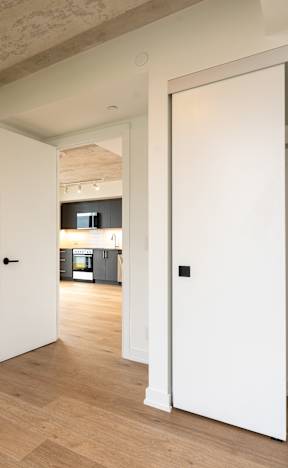 A white door is open to a hallway with wood floors.
