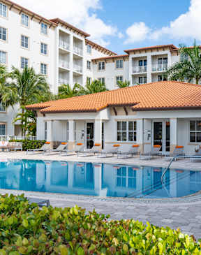 A large white building with a red roof and a pool in front.