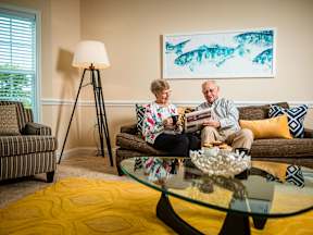 An older couple is sitting on a couch in a living room.