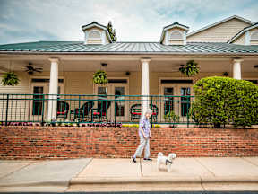 A woman walking her dog in front of a house with a green roof.