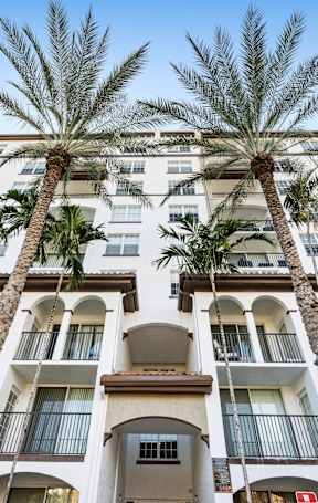 A tall building with balconies and palm trees in front.
