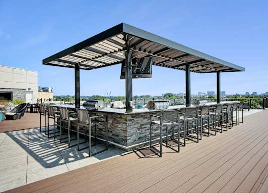 A wooden deck with a bar and chairs under a roof.
