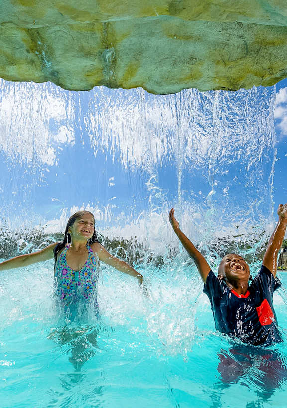 a man and a woman playing under a water shower in a pool