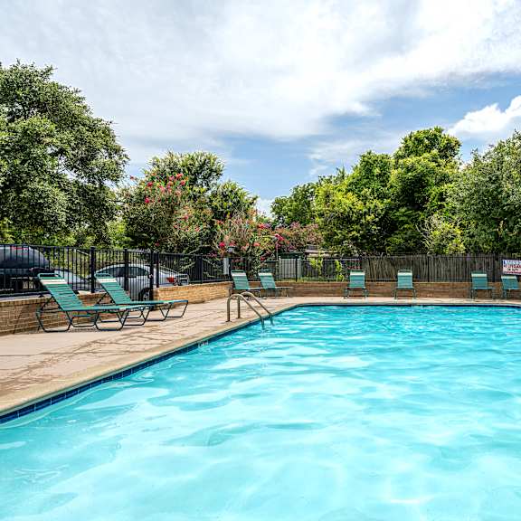A large blue swimming pool surrounded by trees and lounge chairs.