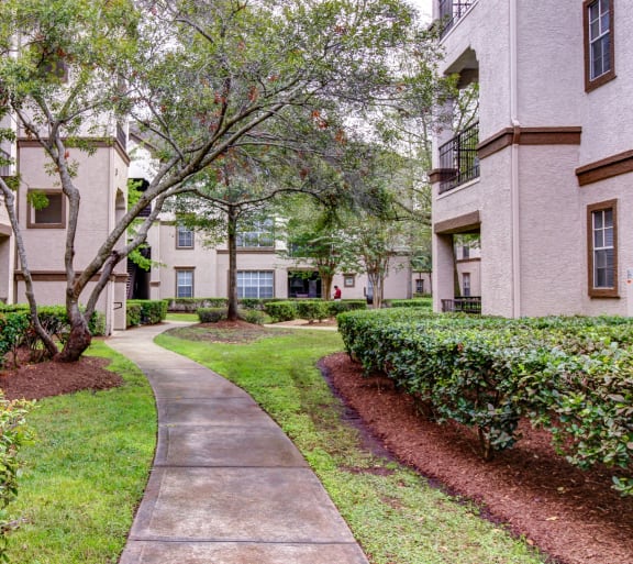 a sidewalk leading to an apartment building with trees and bushes at Stone Creek at Old Farm Apartments, Houston