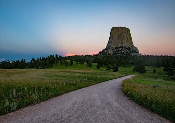 A dirt road leads to a large rock formation in the distance.