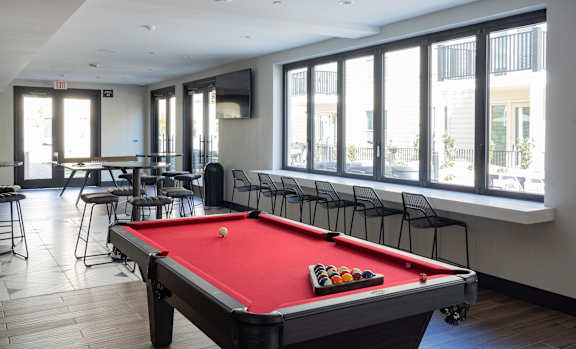 A pool table is in the middle of a room with a TV and a row of chairs.