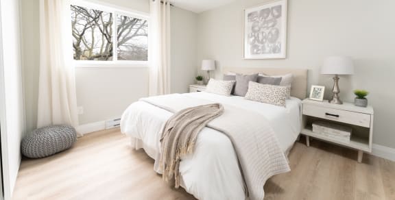 a bedroom with a large window and a bed with a white comforter and pillows