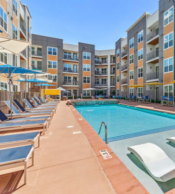 a swimming pool with chaise lounge chairs and umbrellas in front of an apartment building