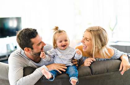 A family of three is sitting on a couch, with the child in the middle being held by the woman.